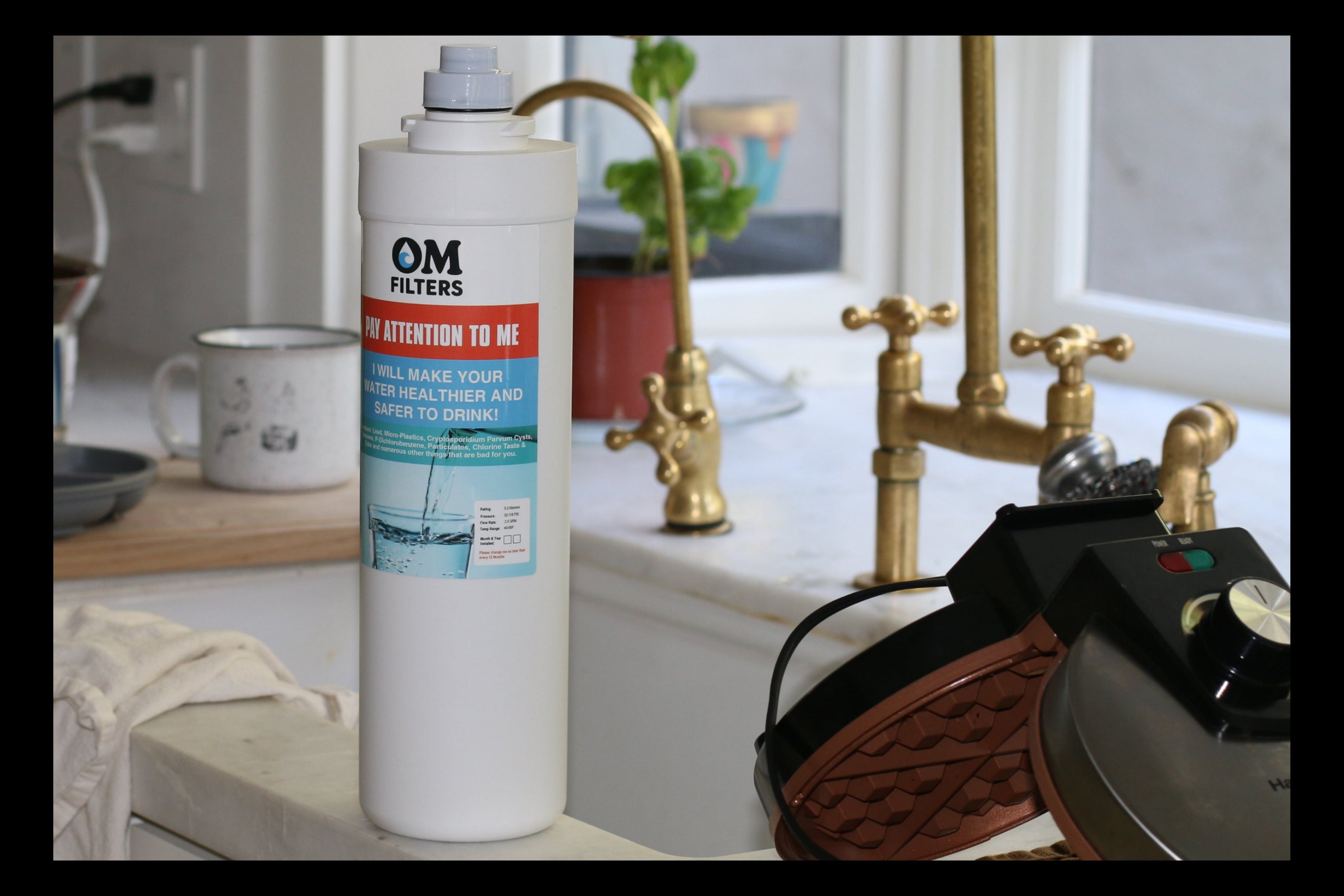 OM Filters water filter cartridge on a kitchen counter with a faucet and various items in the background.